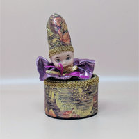 A vintage music box by The San Francisco Music Box Company featuring a porcelain clown head emerging from a floral-patterned base. The clown wears a matching tall hat and a metallic purple ruffled collar.