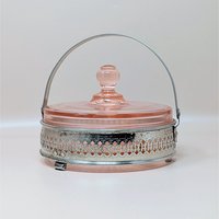 A vintage pink depression glass divided bowl resting in an ornate, silver-tone metal basket with a hinged handle. The matching pink glass lid features a round knob finial.
