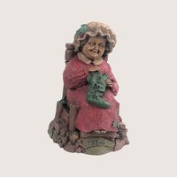 A vintage Tom Clark Cairn Studios resin figurine titled Mrs Claus featuring a woman sitting in a chair knitting a stocking.