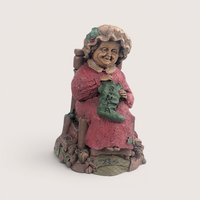 A vintage Tom Clark Cairn Studios resin figurine titled Mrs Claus featuring a woman sitting in a chair knitting a stocking.