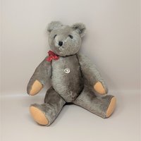 A vintage handmade Felpa teddy bear from Switzerland with grey-brown fur, a red bow, and tan paw pads, shown in a sitting position.