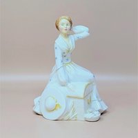 A vintage Royal Doulton figurine titled Summers Day featuring a woman in a white dress with blue star patterns sitting next to a hat and basket
