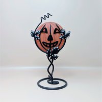 A vintage Department 56 Halloween candle holder featuring a frosted orange glass jack o lantern held within a black metal vine and leaf stand
