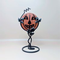 A vintage Department 56 Halloween candle holder featuring a frosted orange glass jack o lantern held within a black metal vine and leaf stand