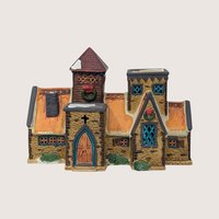 1991 Lemax porcelain village house with stone walls, orange roof, and Christmas wreaths on a plain linen background