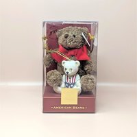 A sealed vintage Lenox American Bears 100th anniversary set on a soft pink background. The clear display box contains a brown plush teddy bear with a red bow and a smaller white porcelain bear ornament wearing a patriotic vest and tiny wire glasses.