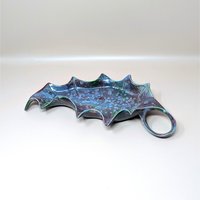 A large vintage studio art pottery leaf dish resting on a soft pink background. The ceramic serving tray is shaped like a stylized holly leaf with a loop handle, covered in a glossy, reactive drip glaze featuring speckled blue and deep purple tones.