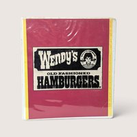 A vintage 1980s Wendy's employee instruction manual in a red three ring binder on a linen background