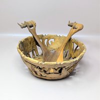 A vintage hand carved wooden safari bowl and matching serving utensils on a soft pink background. The openwork bowl features cutout silhouettes of elephants, while the two wooden servers have handles shaped like small rhinos.