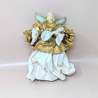 A vintage paper mache and fabric angel tree ornament on a soft pink background. The nine inch tall angel features a metallic gold upper gown, stiffened cream fabric crinkle skirt, soft gold wings, and holds a small blue stringed lute.
