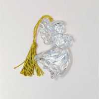 A vintage Gorham crystal angel ornament with a gold tassel on a soft pink background. The fine German glass sculpture features a clear, faceted angel in flight holding a small star, catching the light with brilliant clarity.