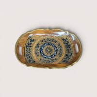 An oval wooden serving tray with intricate black gold and white floral hand painted details on a plain background