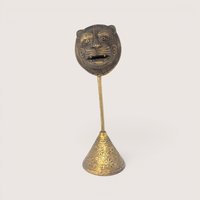 A vintage lost-wax cast brass tribal tiger mask sculpture mounted on a tall etched conical pedestal base.