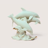 Three ivory porcelain dolphins leaping from a gold trimmed ocean wave on a solid cream colored background