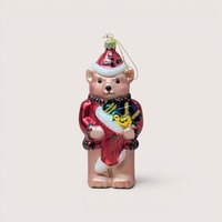 A vintage glass teddy bear ornament wearing a Santa hat and red coat holding a stocking on a plain cream background