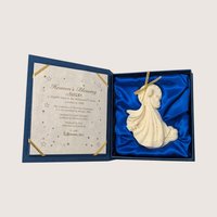 An ivory angel ornament inside a blue satin lined display box with a certificate of authenticity on the lid