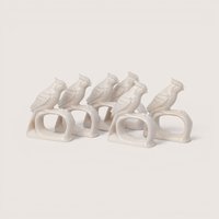 A set of vintage white porcelain napkin rings shaped like crested cardinal birds perched on branches on a plain background