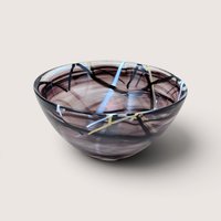 A vintage hand blown purple art glass bowl with abstract black white and yellow swirled lines on a beige background