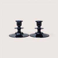 A pair of vintage black glass candle holders with tiered stems and wide round bases on a plain background