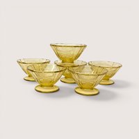 A set of six vintage amber depression glass sherbet cups stacked in a small pyramid on a plain background
