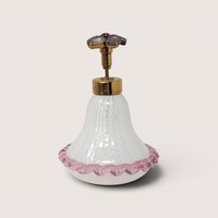 White latticino ribbon glass perfume bottle with a pink ruffled trim and a jeweled flower top on a beige background