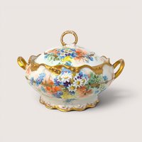 An antique white porcelain covered tureen painted with vibrant wildflowers and heavy gold trim on a beige background