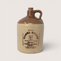A vintage two tone stoneware Daniel Boone bourbon whiskey jug with a cork stopper on a light cream background