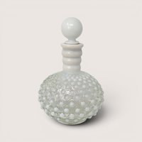 A vintage Fenton white opalescent hobnail cologne bottle with a round ball stopper centered on a light cream background
