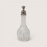 Antique ribbed clear glass perfume bottle with an ornate silver tone floral cap on a neutral background.