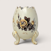 Cream colored footed egg vase with a cracked top edge and yellow rose design on a solid background.