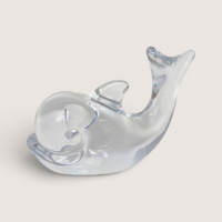 Clear French art glass whale figurine with an upturned tail on a solid background.