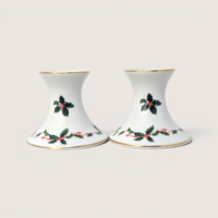 Pair of white ceramic candlestick holders decorated with green holly leaves, red berries, and gold trim.