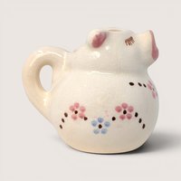 Vintage white ceramic pig shaped cream pitcher with painted pink and blue flowers on a solid background.