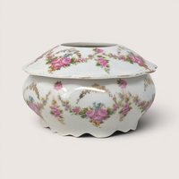 An antique porcelain hair receiver with pink floral swags and gold trim on a plain white background