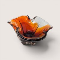 A hand blown art glass bowl with a ruffled rim shifting from amber to deep red on a plain off-white background