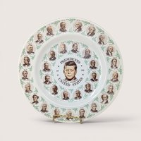 A round ceramic souvenir plate featuring portraits of US presidents with John F Kennedy at the center on a white background