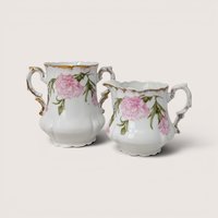 A white porcelain open sugar bowl and creamer set with pink carnation blossoms and gold trim on a plain background