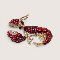 A gold tone lobster brooch encrusted with red rhinestones and red enamel detailing on a plain background