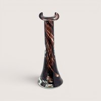 A slender dark brown and amber swirled glass bud vase with a flared base and a crescent shaped rim on a plain background