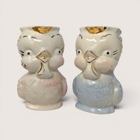 A pair of vintage ceramic owl creamers in pastel pink and blue with gold accents standing side by side