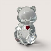 A clear glass seated teddy bear figurine featuring a small red rhinestone heart on its chest centered in the frame.