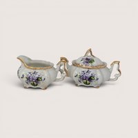 A vintage porcelain creamer and lidded sugar bowl set featuring delicate purple violet bouquets and gold trim.