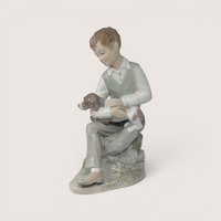 Vintage Zaphir glossy porcelain figurine of a seated boy in a vest gently holding a brown and white puppy.
