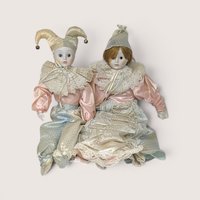 Pair of vintage porcelain Harlequin and Pierrot dolls in pastel pink, blue, and cream satin costumes with lace collars.