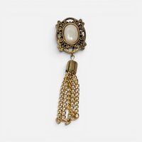 Vintage gold filigree button cover with white cabochon and dangling gold chain tassel on plain background.