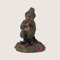 Vintage 1980s Tom Clark Cairn Studios gnome figurine holding a red rose and standing on a base of autumn leaves and acorns.