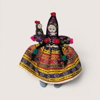 Vintage handmade folk art cloth doll wearing a colorful patterned skirt and holding a baby doll set against a plain linen background.
