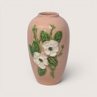 Vintage pink Hull pottery ceramic vase with embossed white flowers and green leaves set against a plain linen background.