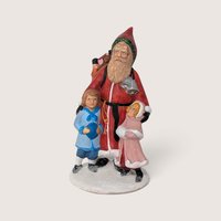 Vintage hand-painted ceramic old world Santa figurine standing with two children on a snowy base.