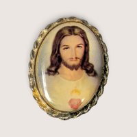 Vintage religious brooch featuring a portrait of the Sacred Heart of Jesus in a decorative scalloped metal frame.